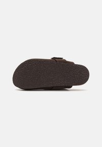 Brune sandaler med en teksturert gummisåle og en justerbar stropp. Designet har en bred tå og en formet fotseng for komfort.
