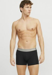 Fekete boxer alsónadrág puha anyagból, szürke elasztikus derékpánttal, amelyen a "JACK & JONES" felirat található. Simás textúra, testhezálló szabás.