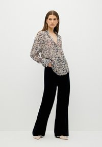 Blusa transparente de manga larga con estampado floral en azul marino sobre fondo crema, con cuello abotonado y corte relajado, combinada con pantalones de terciopelo azul marino.