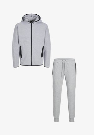 Lichtgrijze capuchonvest met ritssluiting en bijpassende joggingbroek met zwarte ritszakken en trekkoord in de taille.