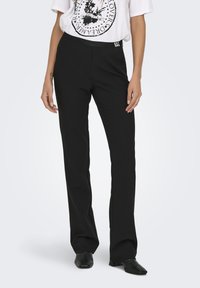Zwarte, rechte broek met een elastische tailleband, gemaakt van een zachte stof. Bevat een klein logo etiket op de tailleband.