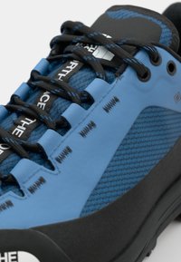 Blue climbing shoe with a textured upper, black rubber outsole, reinforced toe cap, and contrasting black laces. Features branding on the side.