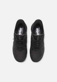 Paire de chaussures de sport noires Skechers sans lacets avec tissu en mesh et lacets élastiques vue de dessus sur fond blanc.