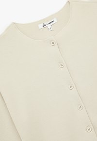 Cárdigan de canalé beige con escote redondeado y cinco cierres de botones. Tejido suave y textura sutil; etiqueta visible en el interior.