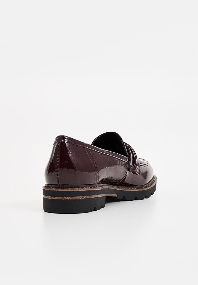 Mocassin en cuir verni bordeaux avec un bout arrondi, des coutures décoratives et une semelle noire basse et texturée. Présente un talon brun contrastant.