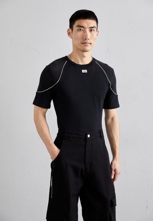 T-shirt noir ajusté à manches courtes avec des accents de couture blanche. Associé à un pantalon cargo noir taille haute avec une poche zippée.