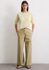 Maglietta a maniche lunghe gialla chiara abbinata a pantaloni cargo larghi color khaki con tasche laterali e chiusura con bottoni anteriori. Tessuto dalla consistenza morbida.