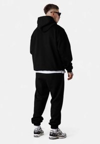 Schwarzer Hoodie und Jogginghose mit bequemer Passform, gerippten Bündchen und layered über einem weißen T-Shirt. Kombiniert mit schwarz-weißen Sneakers.