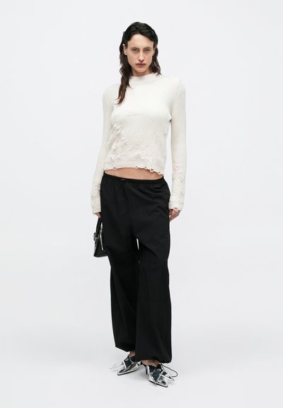 Pulover crem cu dungi rib, cu detalii uzate, asortat cu pantaloni negri largi. Pantofi argintii cu vârf ascuțit și accente; geantă mică neagră.