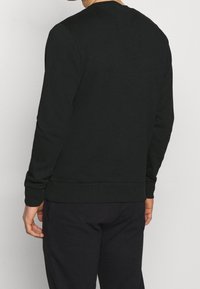 Sudadera negra de manga larga, con un cuello redondo y puños acanalados. El material parece suave con una textura lisa. Diseño simple, sin estampados.