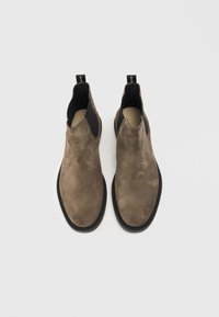 Botas de tobillo de ante marrón con paneles laterales elásticos y tiradores. Punta redondeada y suelas de goma negra en contraste. Textura suave.