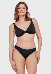 Set di bikini nero con un reggiseno a triangolo morbido con spalline larghe e scollatura profonda, abbinato a slip a vita alta coordinati. Texture liscia.