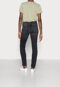 Svarta skinny jeans med hög midja, som har två bakfickor och subtila stygndetaljer. Matchat med en ljusgrön t-shirt och vita sneakers.