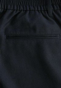 Pantalon en tissu noir avec taille élastique et une poche arrière horizontale fendue unique, montrant des coutures détaillées et la texture.
