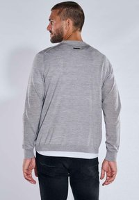 Grauer Langarmpullover mit glatter Textur, runder Ausschnitt und dezentem Nähdetail hinten. Über einem weißen Hemd getragen, kombiniert mit schwarzen Hosen.