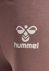 Bordeaux leggings met een wit Hummel-logo en een uniek patroon. De gladde textuur en het aansluitende ontwerp versterken de moderne uitstraling.