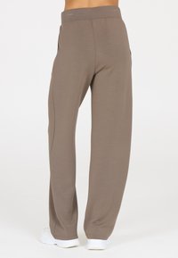 Brown athletic pants with a wide waistband, straight legs, and side pockets; made from a soft, lightweight fabric with a smooth texture.