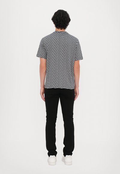 Short-sleeve, navy and white patterned shirt with a round neckline, paired with black pants and white shoes, viewed from the back.