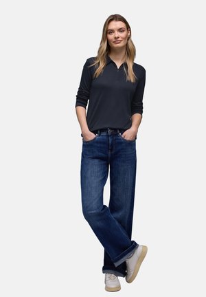 Mørkeblå langærmet poloshirt med lynlås, kombineret med løstsiddende blå jeans og hvide sneakers; afslappet outfit med en løs pasform.