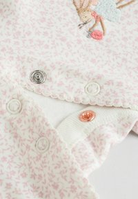 White fabric with a delicate pink floral pattern. Features three snap buttons: silver, white, and rose gold. Scalloped edges detail.