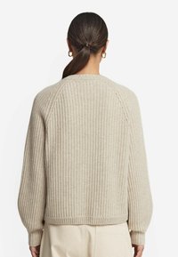 Pull à côtes beige avec un col rond, des manches raglan et une taille ajustée, fabriqué en tissu tricoté texturé pour la chaleur.