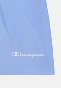 Vêtement de sport bleu à la texture lisse, avec un logo "Champion" blanc en bas, et un ourlet droit avec des coutures soignées.