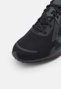 Black athletic shoe with a mesh upper, rubber sole, and contrasting matte accents. Features traditional lacing and a rounded toe design.