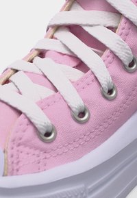 Κοντινό πλάνο ροζ πάνινου αθλητικού παπουτσιού με λευκά κορδόνια περασμένα από μεταλλικά οπές και λευκή λαστιχένια σόλα.