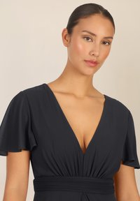 Zwarte jurk met korte vlindermouwen, diepe V-hals enGathered taille. Soepele, lichte stof, minimale details. Zachte textuur.