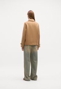 Beige skræddersyet jakke med krave, parret med løstsiddende, lyseblå jeans med et falmet mønster. Ren, minimalistisk design.