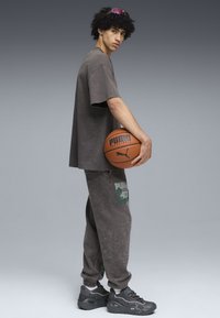 Grå oversized t-shirt og matchende joggers med grafiske accenter, som holder en basketball. Tekstureret stof og mørke sneakers med chunky design.