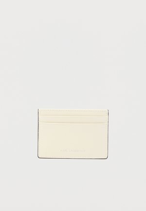 Δερμάτινη θήκη καρτών σε απαλό κρεμ χρώμα, με τέσσερις θήκες για κάρτες, λείο φινίρισμα και ανάγλυφο λογότυπο στο κάτω μέρος. Απλός, ορθογώνιος σχεδιασμός.