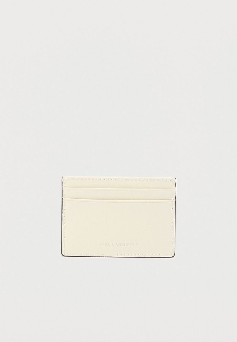 Δερμάτινη θήκη καρτών σε απαλό κρεμ χρώμα, με τέσσερις θήκες για κάρτες, λείο φινίρισμα και ανάγλυφο λογότυπο στο κάτω μέρος. Απλός, ορθογώνιος σχεδιασμός.