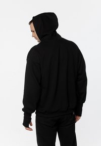 Czarna bluza z kapturem o luźnym kroju, z dużym kapturem, prążkowanymi mankietami i pasem. Materiał wydaje się być miękki i ciężki.