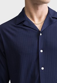 Navy, striped short-sleeve shirt with a notched collar, featuring white buttons and a smooth texture. A subtle sheen adds depth.