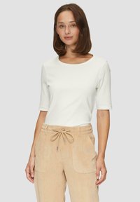 Weißes, geripptes Oberteil mit kurzen Ärmeln, kombiniert mit tanfarbenen kordelgewebten Hosen mit verstellbarem Bund und seitlichen Taschen. Glatte Textur, figurbetontes Design.