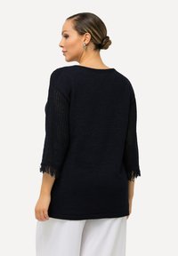 Mörkblå stickad tröja med öppet stickade ärmar och fransdetaljer. Har en rundad urringning och en lös passform.