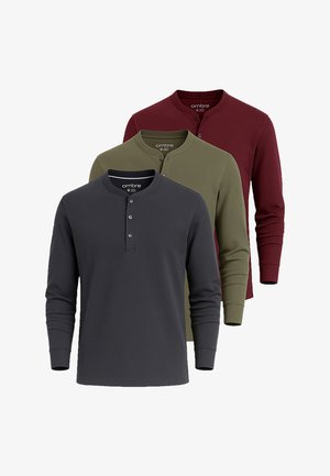 Drie lange mouw henley-shirts in antracietgrijs, olijfgroen en donkerrood, netjes van voren naar achteren gerangschikt met knoopkraag.