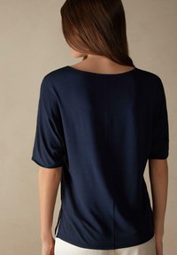 Navyblauw top met korte mouwen, een brede halslijn en zijslits. Zacht, soepel materiaal met een subtiele glans en een centrale achternaad.
