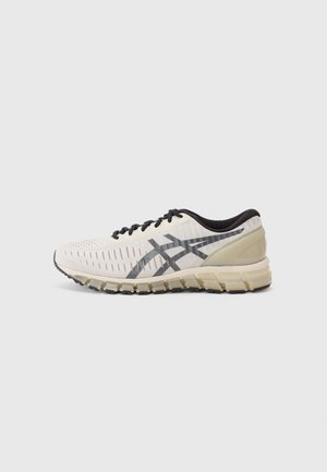 Chaussure de course blanche avec des lacets noirs, un intérieur noir, des bandes de logo grises et une semelle beige épaisse et flexible sur un fond clair.