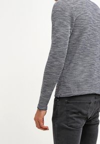 Mörkblå långärmad tröja med texturerad stickning, med rund hals och en något beskuren fåll. Matchad med mörkgrå byxor.