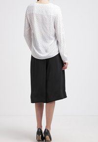 Pitkähihaista valkoista paitaa, jossa on mustia pilkkuja, yhdistetty mustaan polvimittalaiseen hameeseen. Hameella on sileä rakenne ja kevyt kiilto.