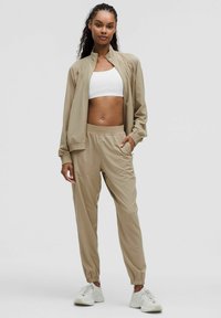 Beige athletic set featuring a zip-up jacket with a textured finish, paired with elastic-waist pants and a white crop top.