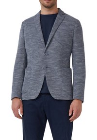 Grau und blau gewobener Blazer mit schlanker Passform, einreihigem Design, zwei Vorderaschen und zwei Knöpfen. Über einem dunklen Hemd getragen.