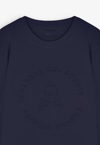 Sweat-shirt bleu marine à col rond avec logo en relief de crâne et os croisés et texte circulaire indiquant "Scalpers Co. Studio" sur le devant.