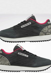Baskets Reebok noires et grises avec doublure rouge, lacets noirs, semelles intermédiaires blanches et accents gris texturés au talon, vues de profil.