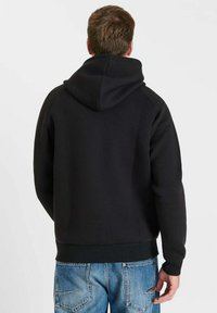 Zwarte capuchonsweatshirt met een zachte textuur, geribbelde manchetten en tailleband. De achterkant heeft een naadloos ontwerp, gecombineerd met lichtblauwe jeans.