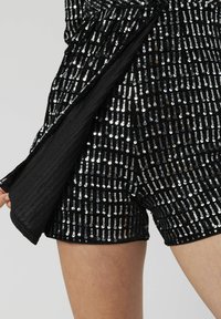 Shorts noirs à paillettes avec une surface texturée et des paillettes argentées disposées en lignes verticales. Le tissu a une finition lisse et brillante.