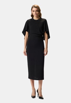 Abito midi nero con silhouette aderente, maniche corte a sbuffo e scollo rotondo decorato con perline. Paio di décolleté nere.