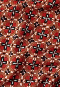 Textil med ett geometriskt blommönster i rött, svart och grönt på en brun bakgrund; mjuk textur med en subtil lyster.